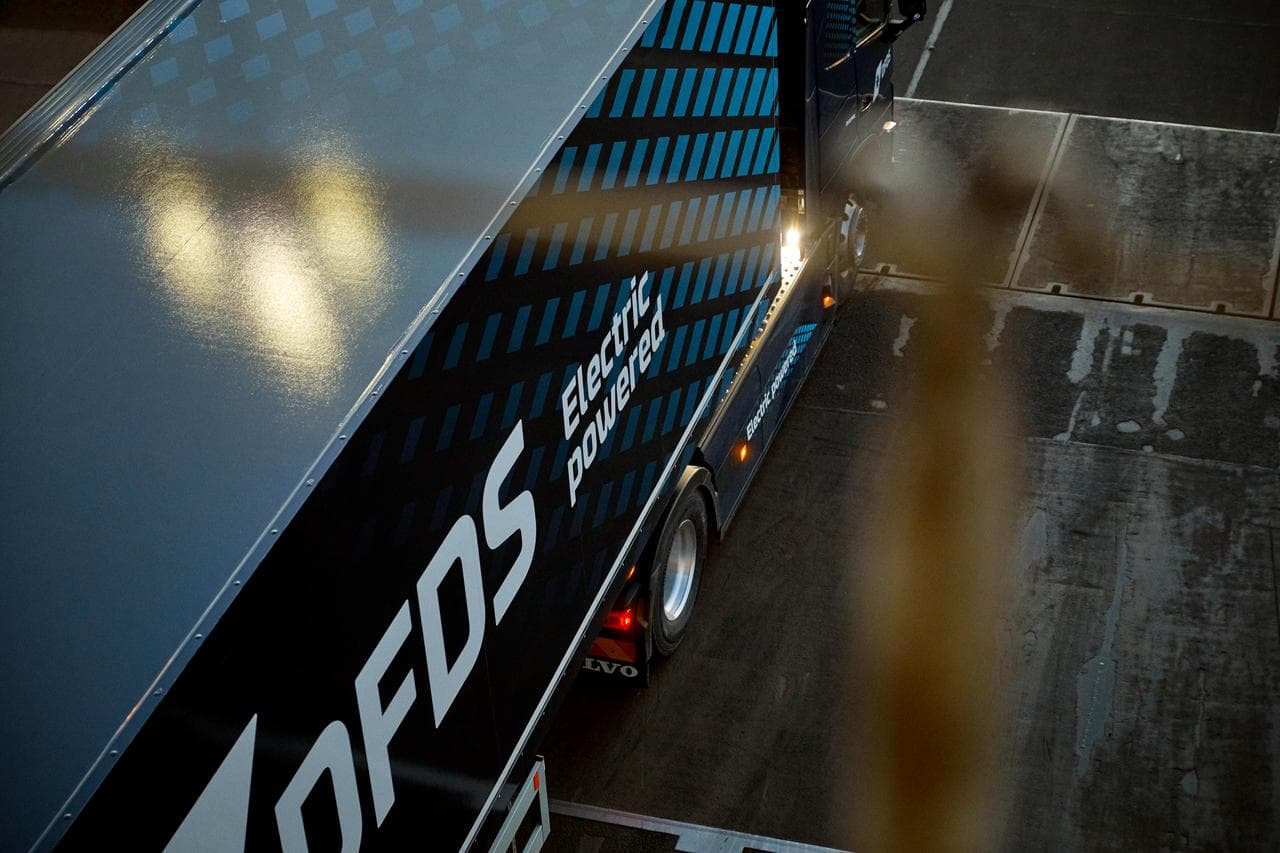A dark blue electric truck, in white DFDS livery as seen from above, driving backwards on board a vessel