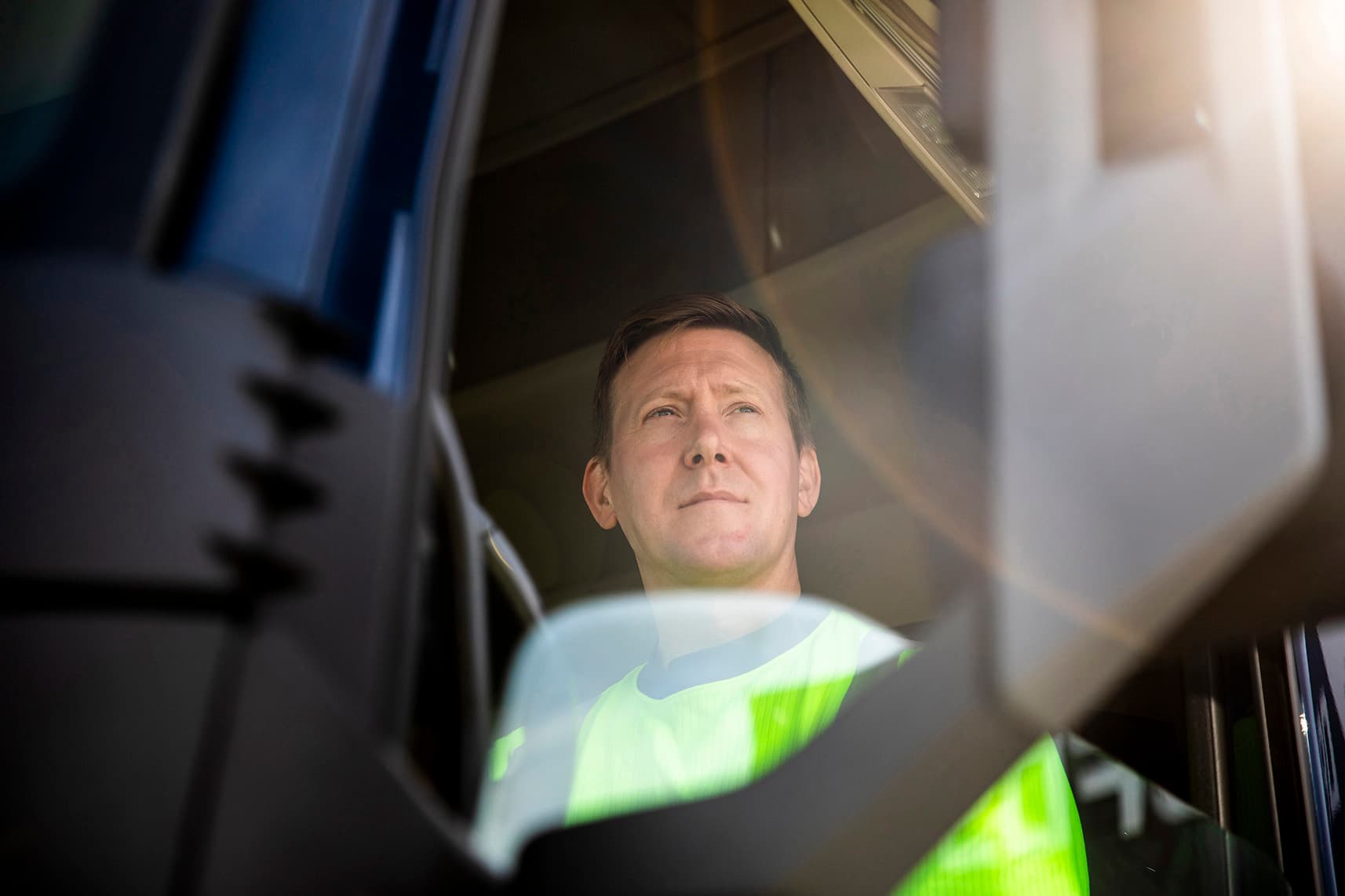 A DFDS truck driver, wearing a high visibility shirt, driving during a sunny day.